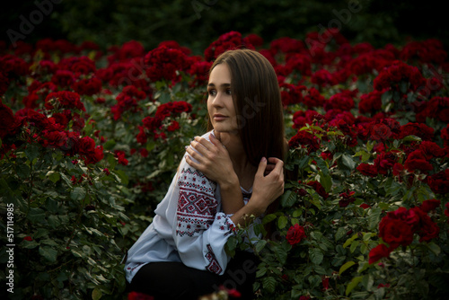  portrait of a woman in  ukrainian white and red embroidery in the evening park with red roses