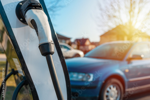 Close up power cord for electric car. Green station.Power supply for electric car battery charging.Blurred car,sunset in the background.Selective focus.Closeup. © ARVD73