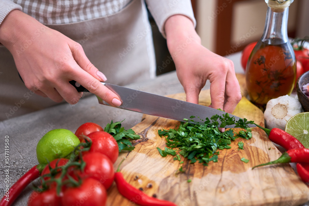 making salsa dip sauce - woman cutting and chopping cilantro or parsley on wooden cutting board