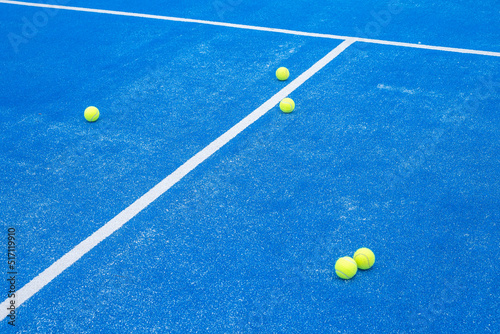 selective focus five paddle tennis balls on a blue paddle tennis court with a net in the background © Vic