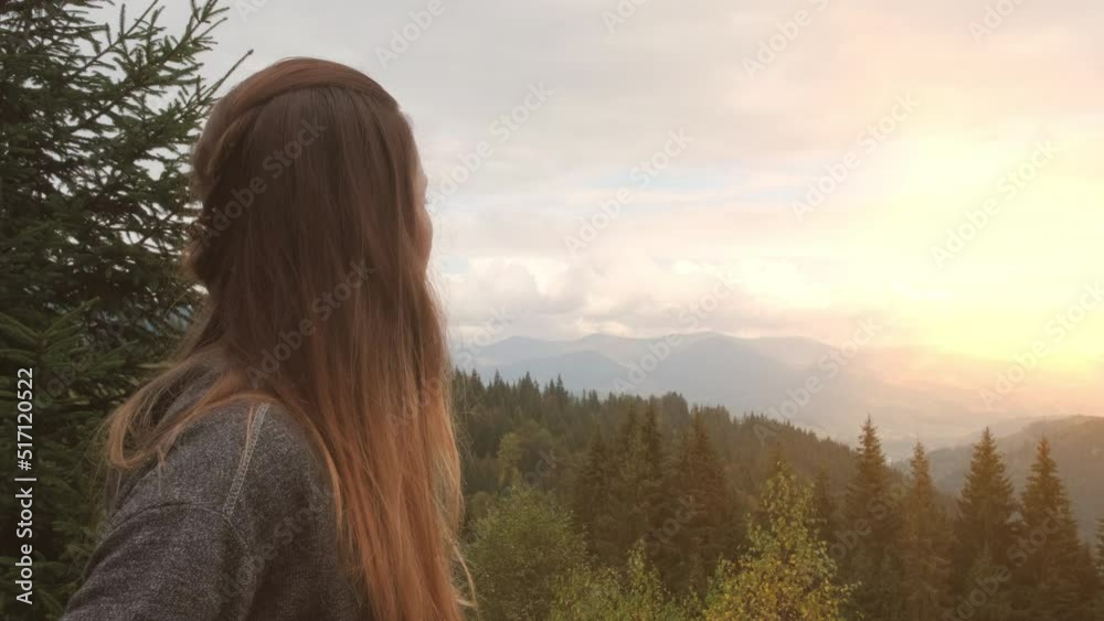 Girl turns her head towards beautiful sunset in forest mountains. Green spruce trees, clouds, bright sun. Carpathians, Ukraine, Europe. Girl turns her head towards beautiful sunset in forest mountains. Green spruce trees, clouds, bright sun. Carpathians, Ukraine, Europe.