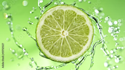 Slice of lime with water splashes on green background.