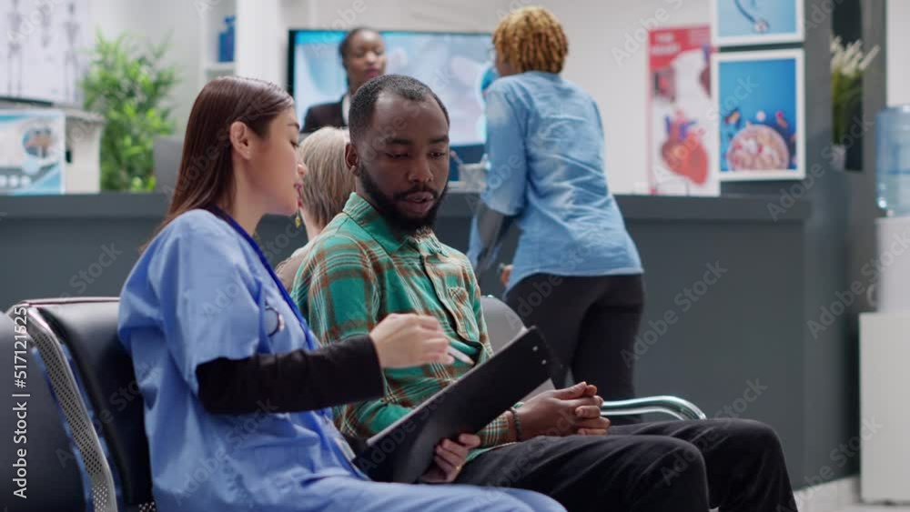 Diverse people talking about disease diagnosis in waiting room at hospital reception lobby. Man and woman doing checkup consultation to help with treatment and healthcare recovery. Handheld shot. Diverse people talking about disease diagnosis in waiting room at hospital reception lobby. Man and woman doing checkup consultation to help with treatment and healthcare recovery. Handheld shot.