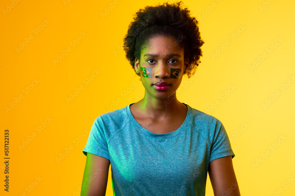 Image of african american female soccer fan with flag of portugal in yellow lighting Image of african american female soccer fan with flag of portugal in yellow lighting