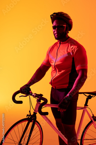 Vertical image of african american male cyclist looking at camera in yellow lighting