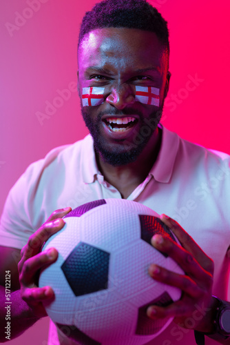 Vertical image of african american male soccer fan with flag of england in neon pink lighting