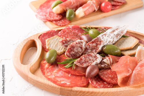 Charcuterie board with variery of sausages - salami, bresaola, proscuitto served with olives and crackers over white table. Menu background with copy space. Traditional italian antipasti