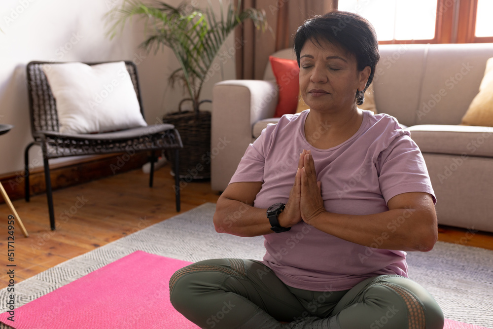 Mature biracial woman with short hair closing eyes and meditating while sitting in living room Mature biracial woman with short hair closing eyes and meditating while sitting in living room