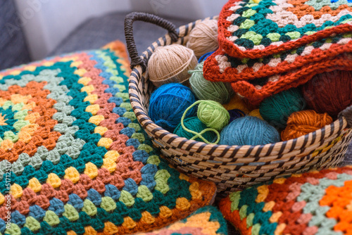 Home made creations. Colorful wool yarns in a straw basket on a couch. Handmade knitting, knit pillows, and a cute atmosphere.
