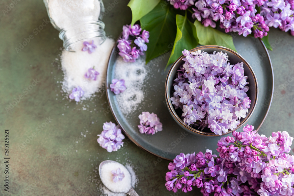 Flavored sugar with lilac flowers in glass jar and branch of beautiful lilac, green concrete background. Edible flowers in cooking and confectionery. Flavoring ingredients. Flavored sugar with lilac flowers in glass jar and branch of beautiful lilac, green concrete background. Edible flowers in cooking and confectionery. Flavoring ingredients.