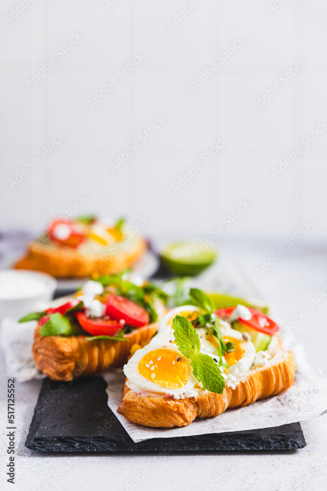 Variety of croissant sandwiches with tomato, cucumber, mozzarella cheese, eggs and mashed avocado with mint and arugula. Open savory sandwiches. Tasty healthy breakfast. Variety of croissant sandwiches with tomato, cucumber, mozzarella cheese, eggs and mashed avocado with mint and arugula. Open savory sandwiches. Tasty healthy breakfast.