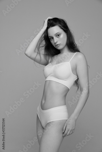 Portrait of young beautiful girl with slim body shape posing in white underwear. Black and white photography aesthetics