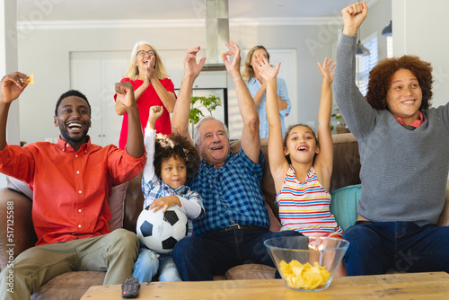 Multiracial multigeneration family with arms raised celebrating victory while enjoying match at home