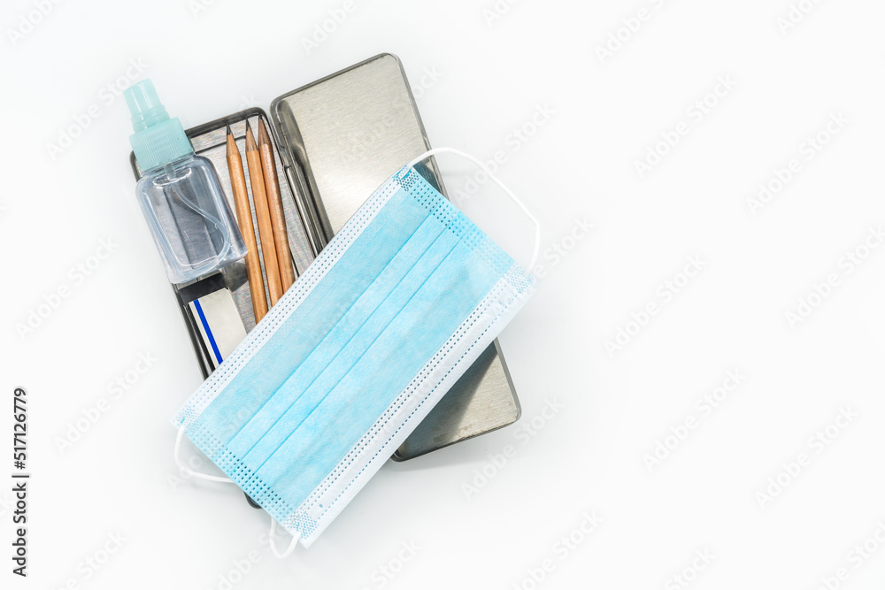 Top view stainless steel pencil box with pencils, medical face mask and a small bottle of alcohol, the isolated image on white background, the concept for back to school in the era of Covid virus. Top view stainless steel pencil box with pencils, medical face mask and a small bottle of alcohol, the isolated image on white background, the concept for back to school in the era of Covid virus.