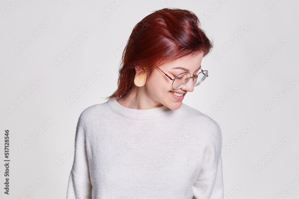 Smiling redhead woman in big eyeglasses with pierced tunnel in ears posing over white background copy space Smiling redhead woman in big eyeglasses with pierced tunnel in ears posing over white background copy space
