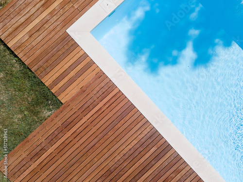 Drone flight over pool with nice wooden terrace surrounded by green lawn in beautiful garden