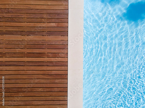 Drone flight over pool with nice wooden terrace surrounded by green lawn in beautiful garden