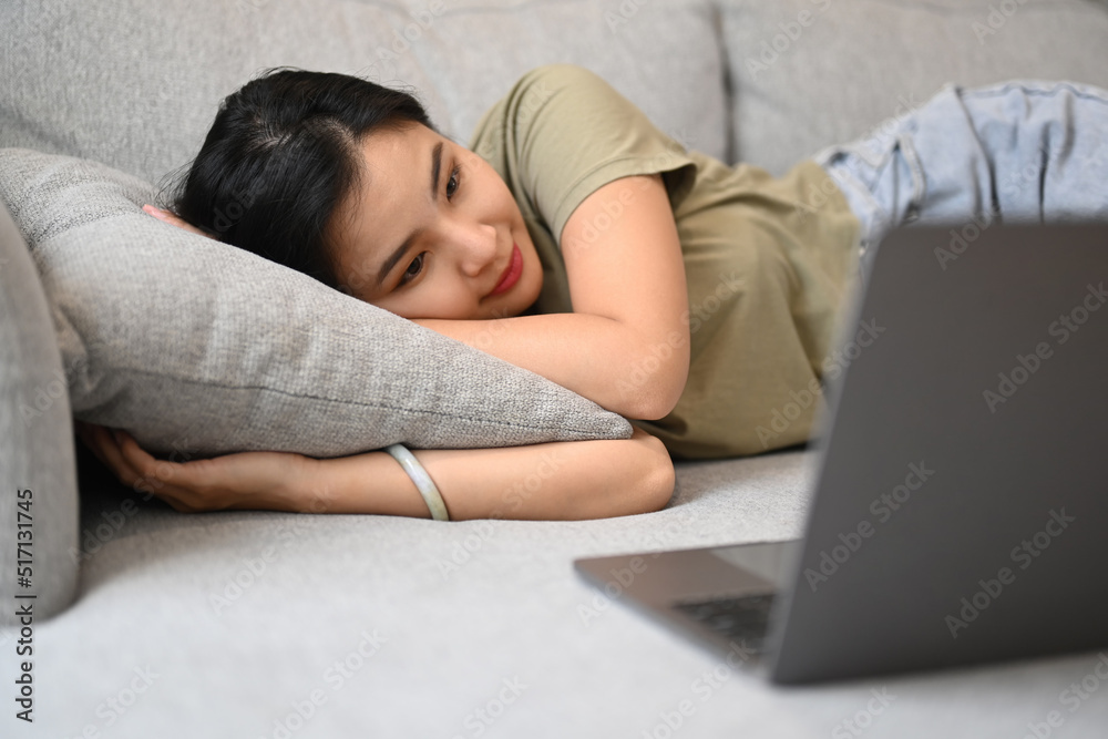 Casual young woman lying on couch and watching movie or communication through video chat on laptop Casual young woman lying on couch and watching movie or communication through video chat on laptop