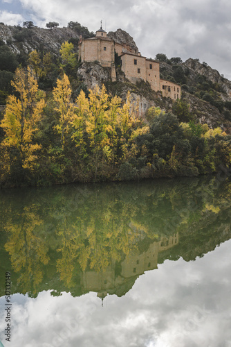 Fototapeta Naklejka Na Ścianę i Meble -  Hermitage of San Saturio at the top of the hill in autumn with yellow trees and at his feet the Duero river where some trees are reflected. Soria, Spain