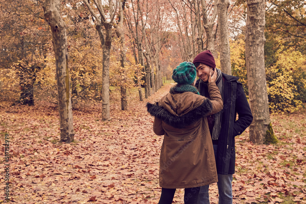 Caucasian white back girl in front of her boyfriend looking into each other's eyes in love in a park in autumn with the ground full of brown fallen leaves Caucasian white back girl in front of her boyfriend looking into each other's eyes in love in a park in autumn with the ground full of brown fallen leaves