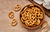 top view or flat lay mini salted pretzel in a wooden bowl with a spoon and fork on wood table background.