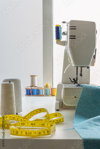 sewing machine next to a tape measure and some spools of colored thread. on top of a white table in a sewing workshop. close-up vertical
 photo