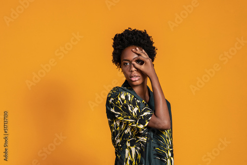Young African American woman with short hair dressed in a summer shirt posing on an orange colored background