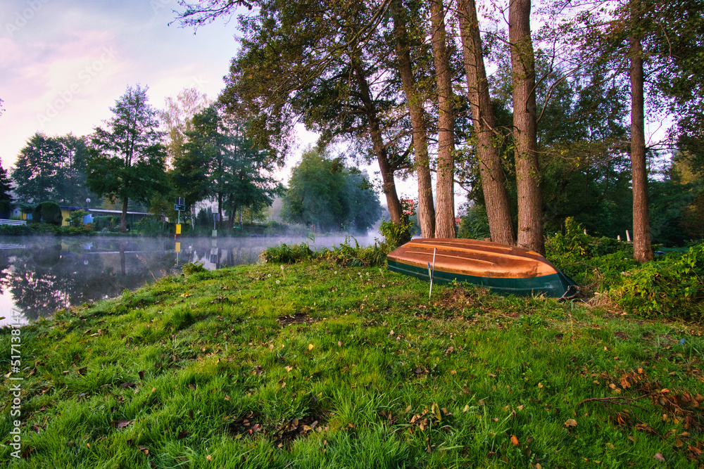 At dawn a sunrise, with fog on the river and warm light atmosphere. Boat on the meadow