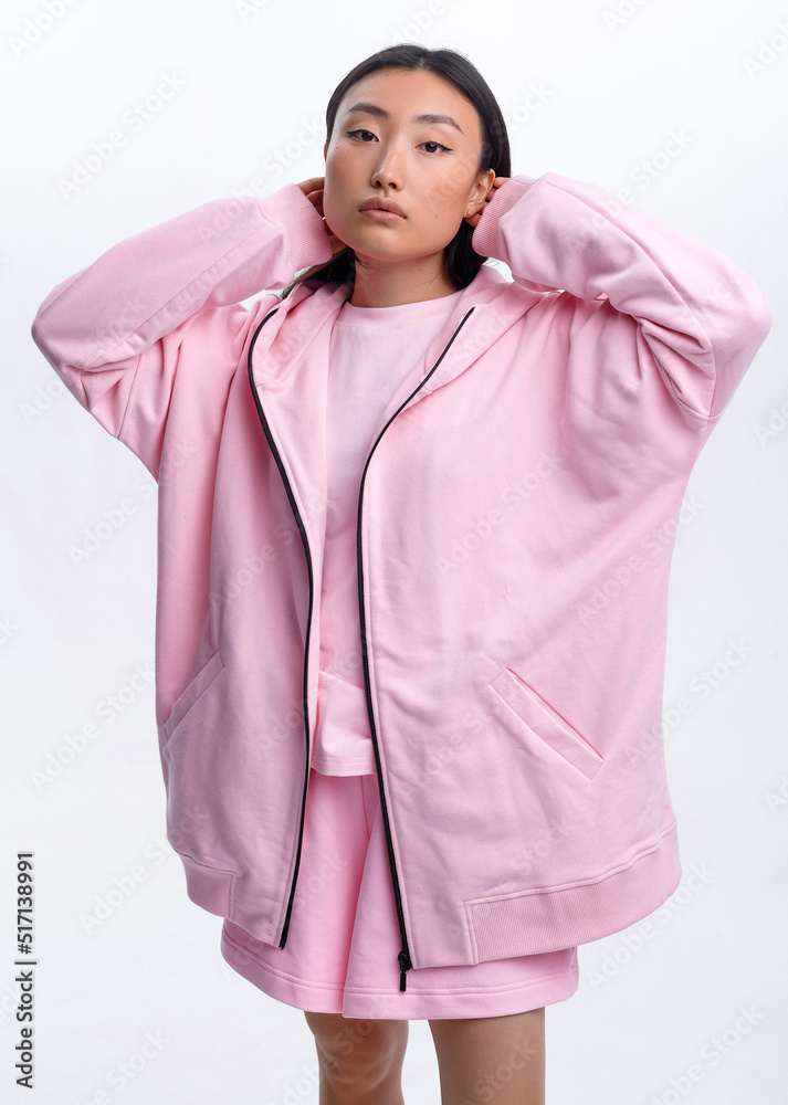 Fototapeta premium Beautiful Asian girl in a pink casual tracksuit posing against a white wall in a photo studio