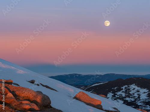 Cairngorms at sunset with colorful Belt of Venus and the rising moon in the sky during the winter season viewed from slopes of Carn Gorm