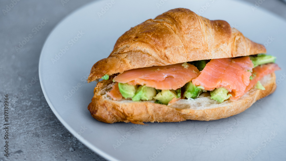 Fresh croissant with salmon and avocado. Healthy and tasty breakfast. Healthy diet. Close-up. Fresh croissant with salmon and avocado. Healthy and tasty breakfast. Healthy diet. Close-up.