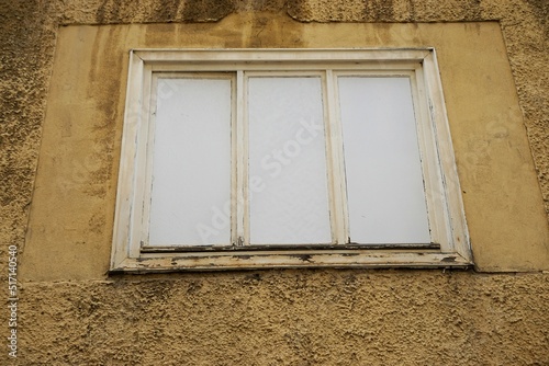 Alte verwitterte braun-gelbe Hausfassade mit Fenster in weißem Holzrahmen und weißer Holzplatte von verlassenem geschlossenem Haus photo