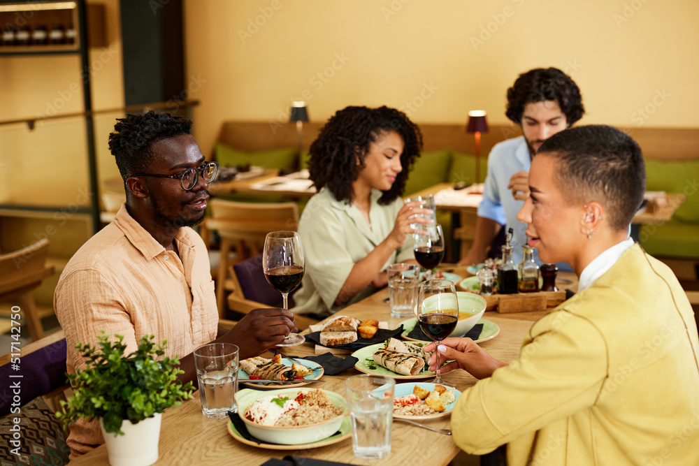 Four friends are sitting in the restaurant, drinking wine, talking, and enjoying dinner. Four friends are sitting in the restaurant, drinking wine, talking, and enjoying dinner.