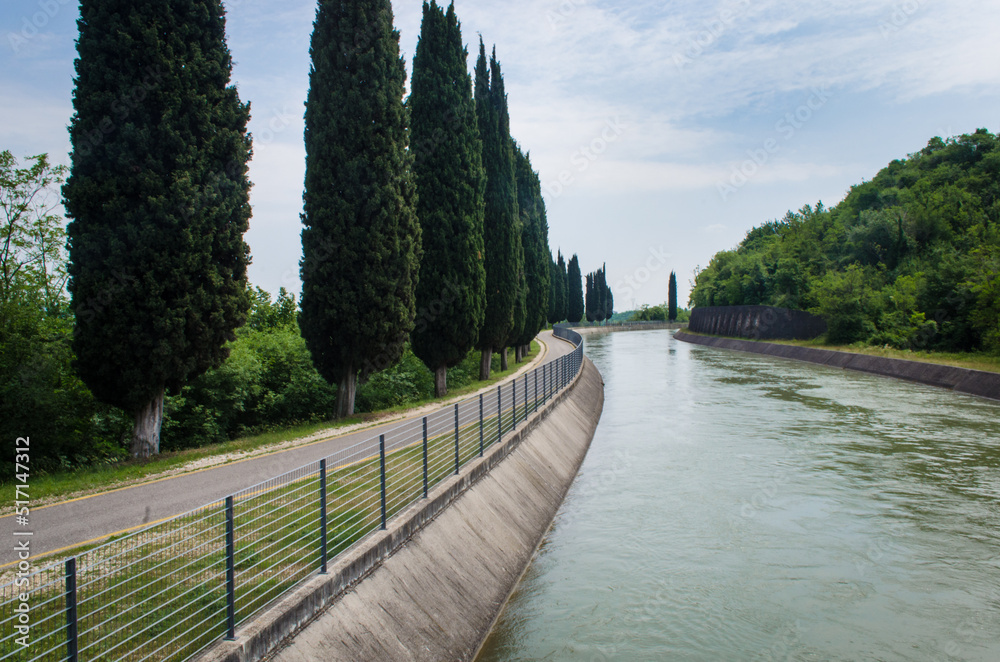 La pista ciclabile dell'Adige fra un canale e un filare di cipressi lungo la Via Postumia, cammino che parte da Aquileia e arriva a Genova