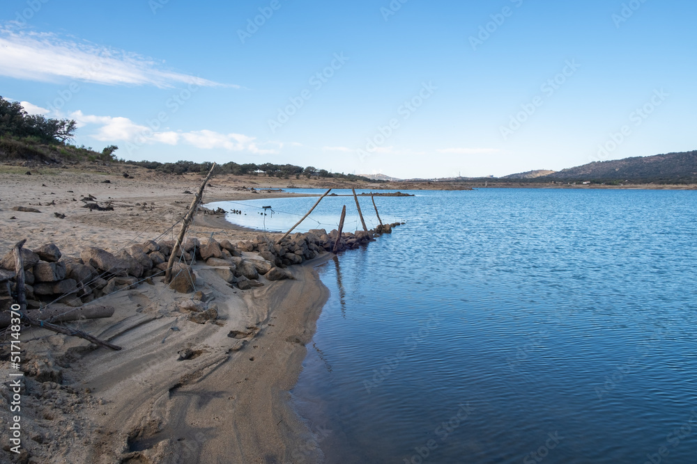 A submerged and weathered barbed wire fence enters the water of a lake.