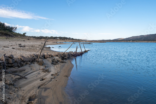 A submerged and weathered barbed wire fence enters the water of a lake.