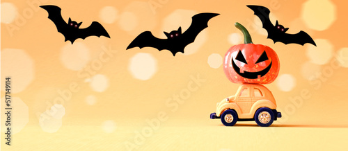 Fototapeta Naklejka Na Ścianę i Meble -  Toy car with funny pumpkin on the roof and bats on orange background. Space for text. Halloween background