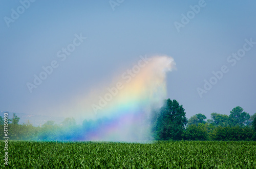Il getto d'acqua di un irrigatore agricolo crea un arcobaleno quando è colpito dai raggi del sole photo