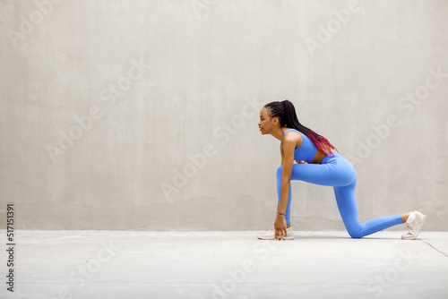 Black american fitness model trains in the morning outdoors against a gray wall.