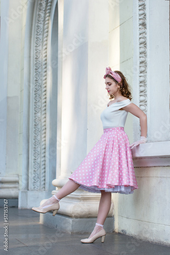 Bright color photo of a beautiful girl with curly hair in a retro style of the 50s in a pink polka dot skirt, while walking through the streets of the city, shot with depth of field and bokeh