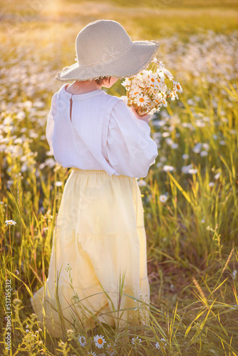young girl holding bunch of chamomile on the summer field