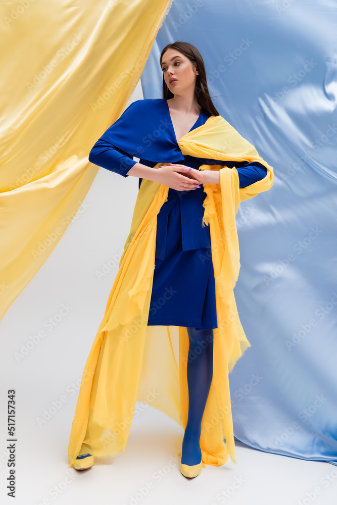 full length of young ukrainian model in color block dress posing near blue and yellow curtains.