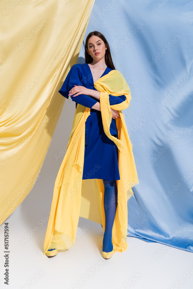 full length of confident young ukrainian woman in color block dress posing near blue and yellow curtains.