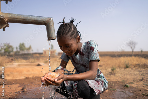 Young African girl happily looking at her handful of water flowing from the village well after a long dry season