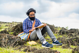 Thoughtful beard author seriously writing novel while sitting on top of hill - conept of artist, creativity and imagination