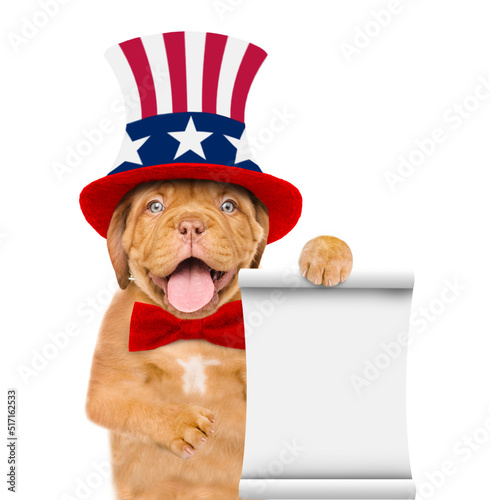 Happy Mastiff puppy wearing like Uncle Sam with sunglasses shows empty list. isolated on white background © Ermolaev Alexandr