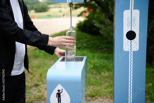 Man refilling his water bottle at the city. Free public water bottle refill station. Sustainable and green city. Male in black coat. Tap water to reduce plastic bottle usage. Drinking water dispenser photo