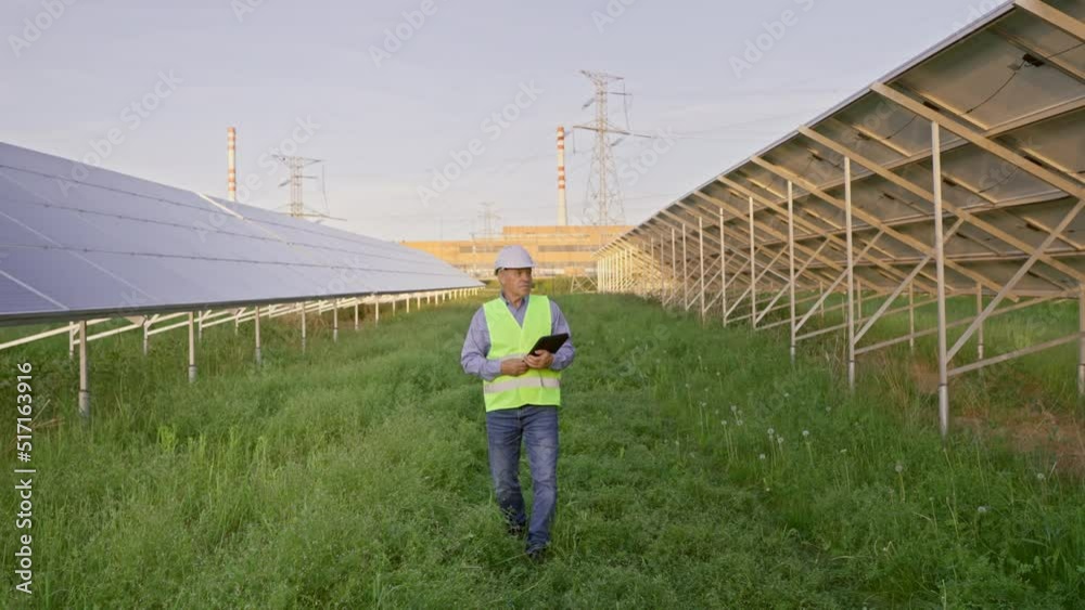 Industrial senior man engineer in uniform walking through solar panel field for examination Industrial senior man engineer in uniform walking through solar panel field for examination