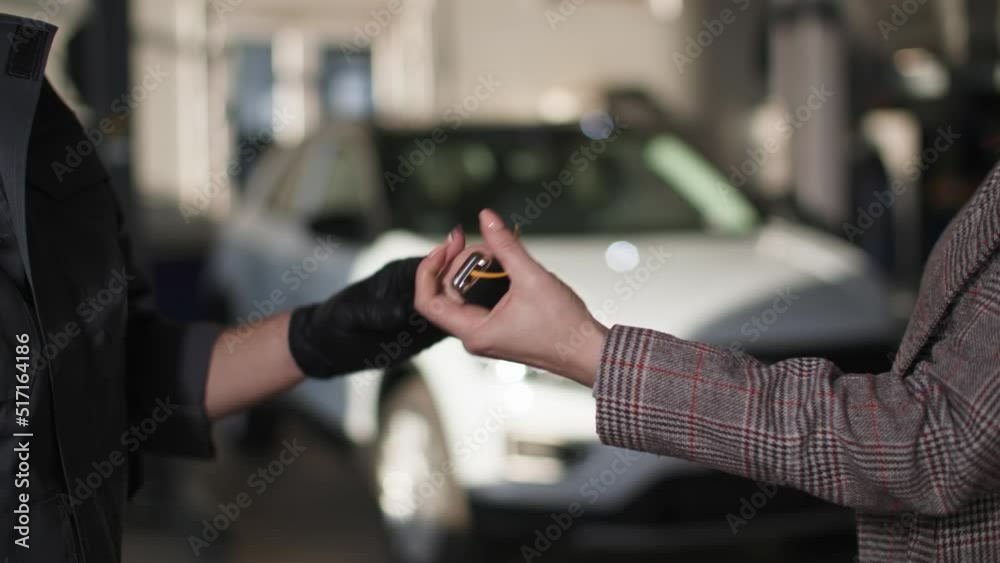 auto mechanic handing over car keys to a female client after repair and shaking hands close-up against the background of automobile at a service station