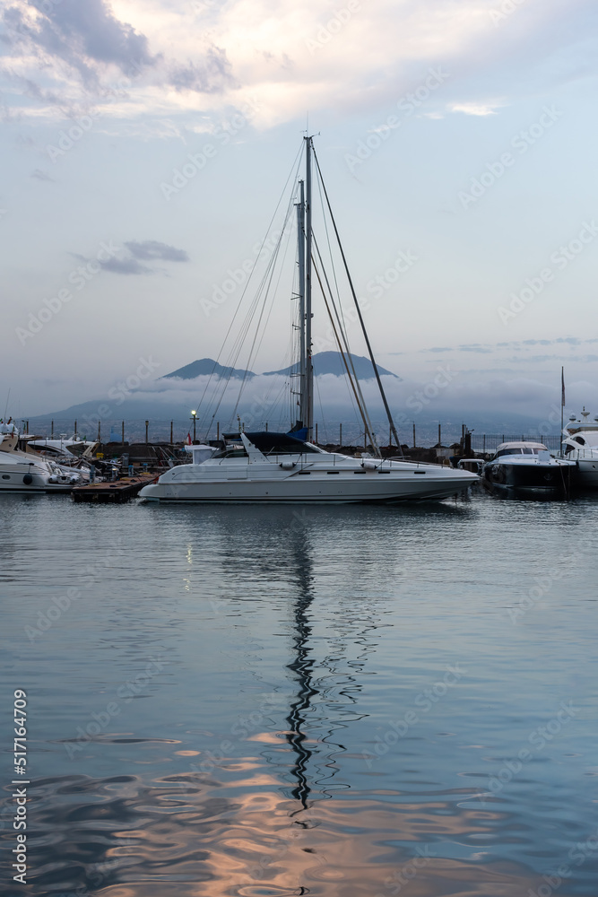 Fototapeta premium Sailboat in harbor on a summer evening with Mount Vesuvius in the background, Naples, Italy